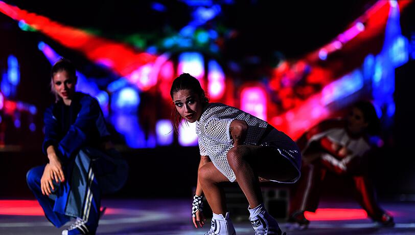 Drei Eiskunstläuferinnen zeigen vor einer bunten Lichtkulisse eine dynamische Performance Drei Eiskunstläuferinnen zeigen vor einer bunten Lichtkulisse eine dynamische Performance