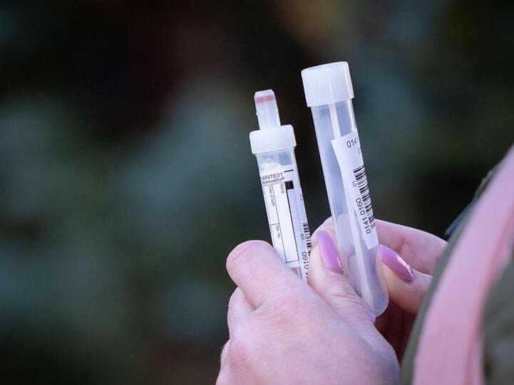 Eine Patientin in Berlin mit zwei Teströhrchen in der Hand für einen Abstrichtest und eine Blutprobe.