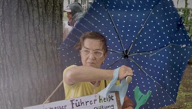 Mit Schirm, Schild und Wut auf Bill Gates: Diese Demonstrantin sucht unter einem Baum Schutz vor dem schlechten Wetter. Mit Schirm, Schild und Wut auf Bill Gates: Diese Demonstrantin sucht unter einem Baum Schutz vor dem schlechten Wetter.