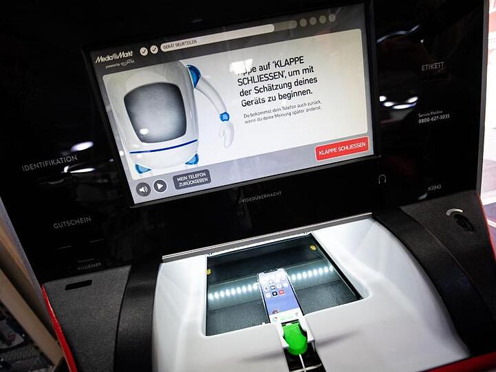 Ein Handy liegt in dem optischen Mechanismus eines "EcoATM" in einer MediaMarkt Filiale. Foto: Lino Mirgeler