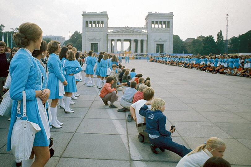 Hostessen und Kinder bilden ein Spalier auf dem Münchner Königsplatz im Rahmen der Eröffnungsfeierlichkeiten der Olympischen Spiele 1972. Diese Veranstaltung sollte die Stadt für immer verändern und bereichern.