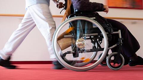 Ein Pfleger eines Pflegeheims schiebt eine Bewohnerin in einem Rollstuhl. Foto: Tom Weller/dpa