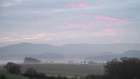 Blick über eine neblige Landschaft in Itzgrund mit Morgenrot am Himmel.