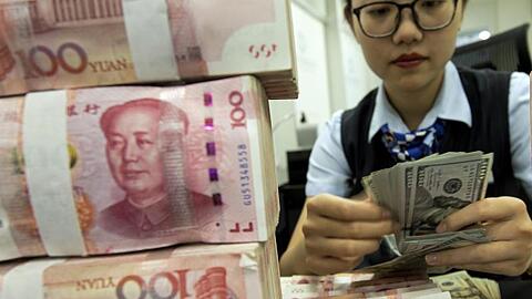 Eine Bankmitarbeiterin in Hai'an zählt US-Dollar-Banknoten neben einem Stapel von chinesischen 100 Yuan-Banknoten. Seit mittlerweile elf Handelstagen ist Chinas Währung auf Talfahrt.