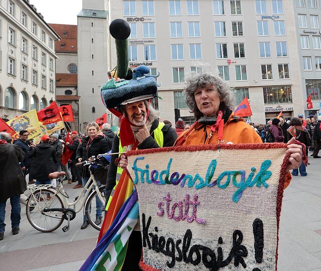 Einen gehäkelten Panzer auf dem Kopf und einen Friedens-Teppich in der Hand: Ein Münchner Ehepaar, das seit vielen Jahren an den Protesten gegen die Sicherheitskonferenz teilnimmt.