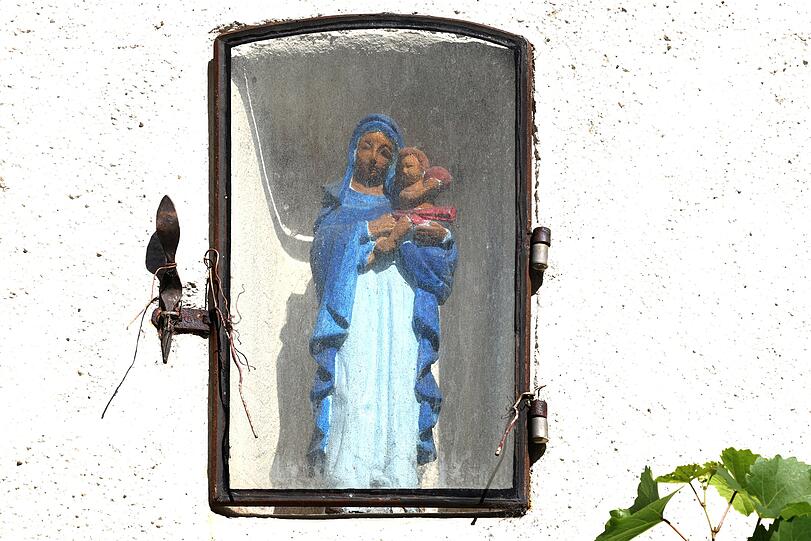 Eine alte Hausmadonna, geschützt hinter Glas.