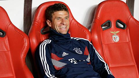 Thomas Müller sitzt vor dem Spiel lachend auf der Bank.