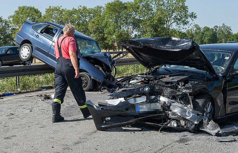 Feuerwehrleute stehen am 27.07.2013 auf der A96 bei Landsberg am Lech neben einem Unfallfahrzeug. Zuvor war ein 76-jähriger Rentner in den BMW eines entgegenkommenden Mannes gefahren.