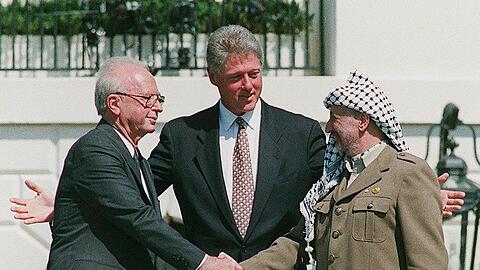Ein Handschlag, der die Hoffnungen auf einen Frieden zwischen Israel und den Palästinensern symbolisiert: Der damalige Ministerpräsident von Israel, Izchak Rabin (l), und Jassir Arafat (r), damaliger Vorsitzender der Palästinensischen Befreiungsorganisation PLO, geben sich im Beisein von Ex-US-Präsident Bill Clinton die Hand.