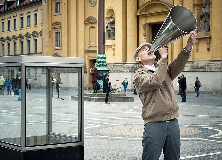 Nach Stationen in Rotterdam und New York präsentieren Elmgreen & Dragset ihre Performance "It's Never Too Late To Say Sorry" auf dem Münchner Odeonsplatz: Täglich um 12 Uhr mittags nimmt ein Mann ein Megaphon aus einem fest installierten Glaskasten und ruft den Satz "Es ist niemals zu spät, sich zu entschuldigen".