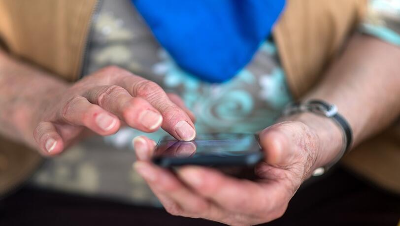 Eine Seniorin tippt auf ihrem Smartphone. Das kann dabei helfen, nach einem Unfall den Notruf zu wählen - ohne es überhaupt in den Händen halten zu müssen.