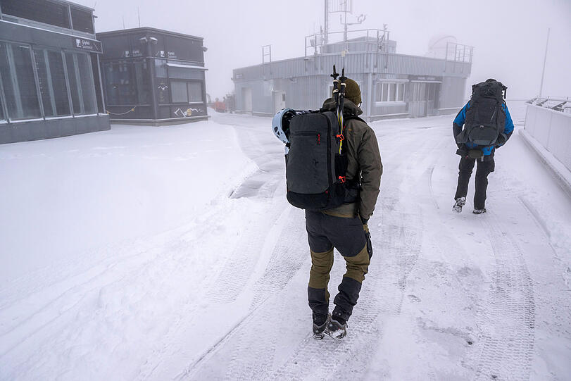 Zwei Bergsteiger laufen bei Schneefall über die Aufsichtsplattform der Zugspitze.
