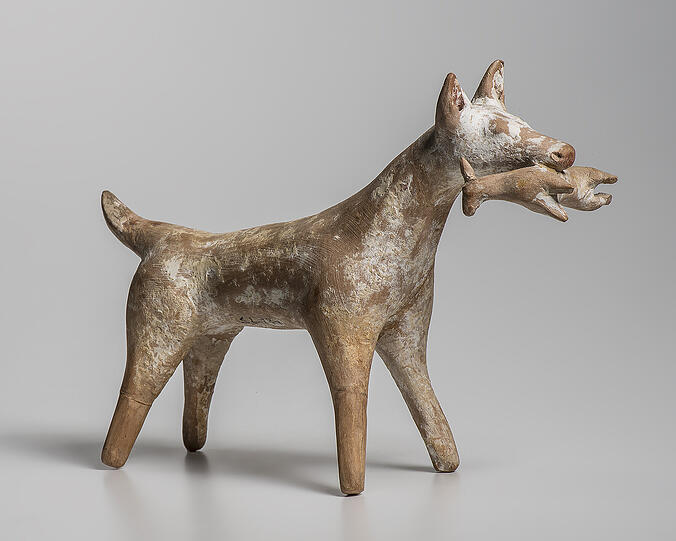 Jagdhund mit Beutetier im Maul. Die Jagd war das beliebteste Freizeitvergnügen der Elite. Nur diese konnte es sich leisten, Zeit und Geld in die Ausbildung der nötigen Hunde zu investieren. Ein gut trainierter Hund war daher auch ein Statussymbol. Statuette eines Hundes aus Böotien, Ton, 5. Jh. v. Chr.