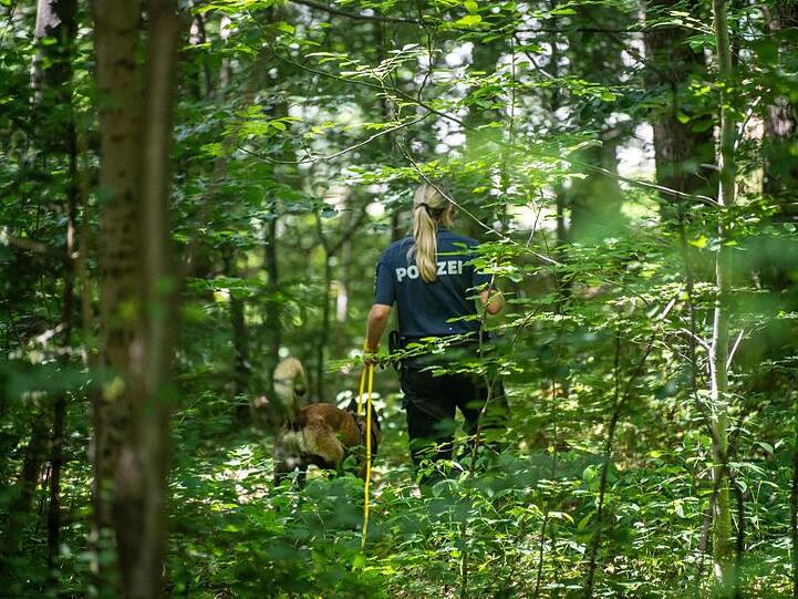 Eine Polizistin sucht mithilfe eines Suchhundes in einem Waldstück nach Hinweisen.