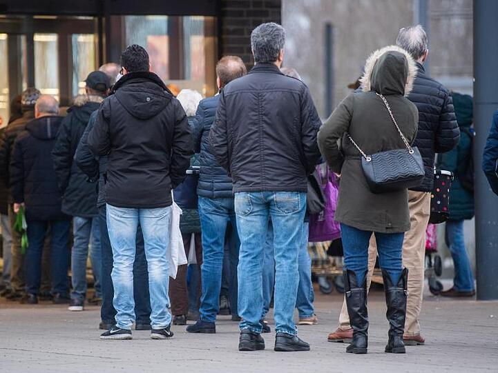 Kunden stehen am frühen Morgen kurz vor Öffnung vor einem Aldi-Markt.