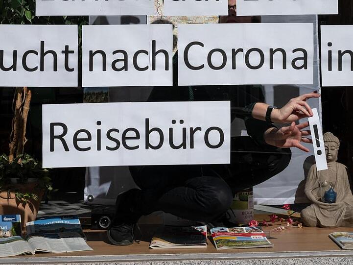Ein Mitarbeiterin klebt Blätter mit der Aufschrift &bdquo;Bucht nach Corona im Reisebüro&ldquo; in das Schaufenster. Foto: Bernd Thissen/dpa