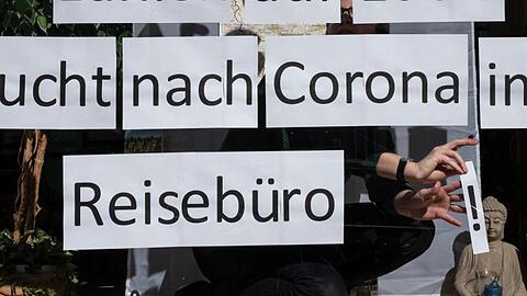 Ein Mitarbeiterin klebt Blätter mit der Aufschrift &bdquo;Bucht nach Corona im Reisebüro&ldquo; in das Schaufenster. Foto: Bernd Thissen/dpa