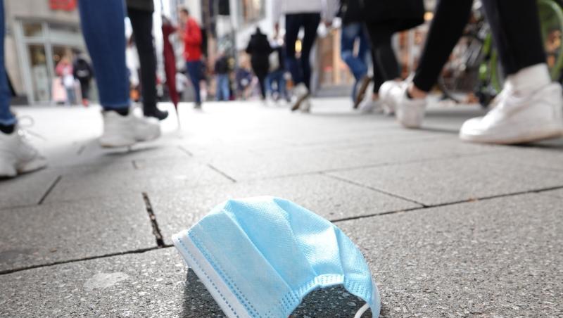 In der Fußgängerzone der Kölner Innenstadt gehen Menschen an einer auf dem Boden liegenden Mund-Nasen-Bedeckung vorbei.