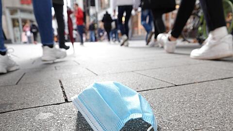 In der Fußgängerzone der Kölner Innenstadt gehen Menschen an einer auf dem Boden liegenden Mund-Nasen-Bedeckung vorbei.