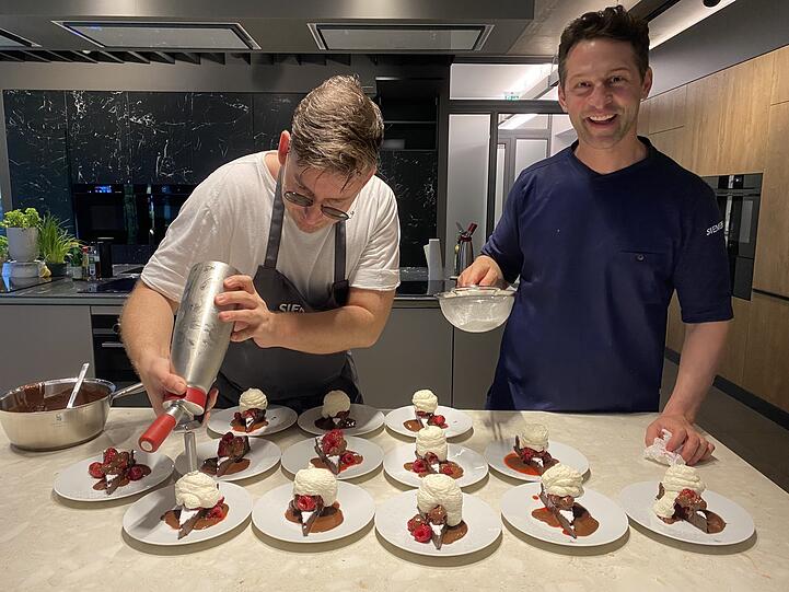 Alexander Kumptner (r.) und sein Kollege springen zwischen Siemens-Öfen und Herdplatten hin und her, dass es eine Freude ist. Am Ende werden die köstlichen Schokokuchen gepudert und dann über München und die Welt geplaudert.