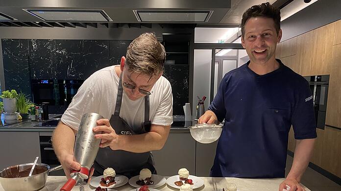 Alexander Kumptner (r.) und sein Kollege springen zwischen Siemens-Öfen und Herdplatten hin und her, dass es eine Freude ist. Am Ende werden die köstlichen Schokokuchen gepudert und dann über München und die Welt geplaudert.