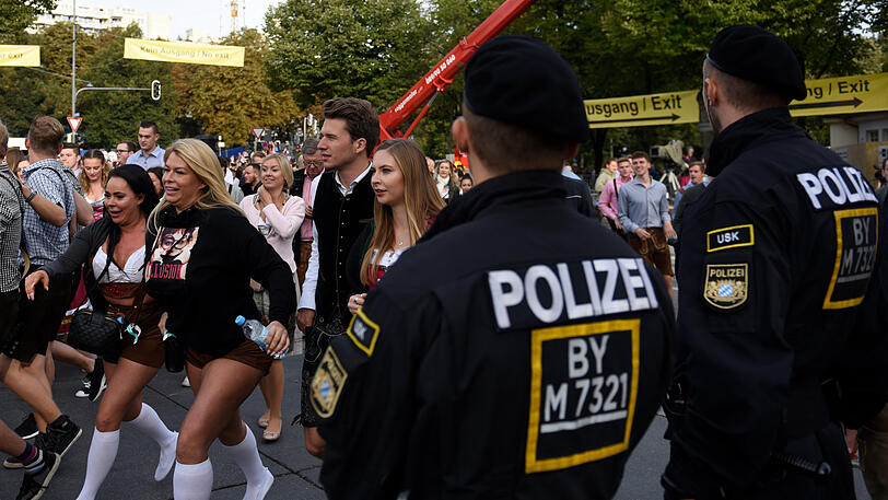 Polizisten stehen am Haupteingang der Wiesn. Fragwürdig: Das Oktoberfest-Outfit der beiden Damen zur Linken.