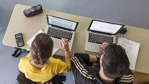Ein Sch&uuml;ler und eine Sch&uuml;lerin sitzen in einem Klassenzimmer vor zwei Computern. In M&uuml;nchen liegt die st&auml;dtische Schul-IT im Verantwortungsbereich einer hundertprozentigen Tochtergesellschaft der Landeshauptstadt.