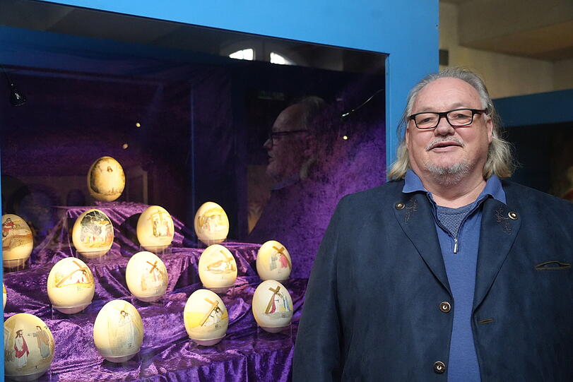 J&uuml;rgen Milla vor einem Satz k&uuml;nstlicher Strau&szlig;eneier, die er mit dem Kreuzweg bemalt hat.