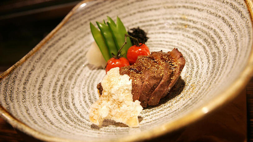 4. Gang: Hochrippe vom Black-Angus-Rind mit Ingwer und japanischem Bergpfeffer. Eine feine Fettmarmorierung zeichnet das zarte Fleisch des Black Angus aus; mit einer Ingwer-Teriyakisauce zubereitet und mit einer Tempuraflocke garniert kommt es im Matsuhisa zum Gast. Im Glas begleitet wird das Rind vom eleganten Cabernet Sauvignon &bdquo;Saurus&ldquo; vom Weingut Familia Schroeder in Argentinien, der eine würzige Nase mit Waldbeeren und Anklänge an Kaffee und Vanille mitbringt.