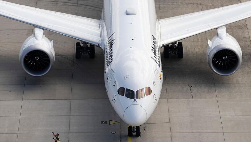 Ein Vorfeld-Arbeiter geht auf einem Flughafen an einem startbereiten Jet der Lufthansa vorbei.