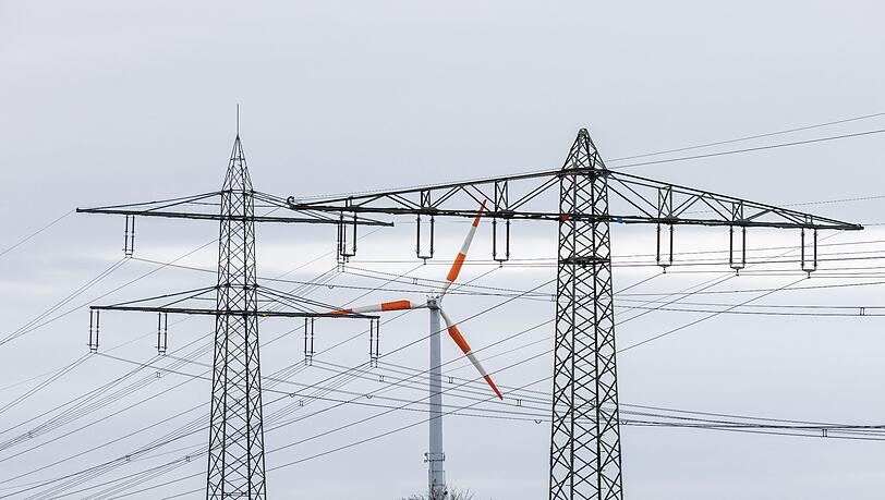 Ein Windrad steht neben dem Mast einer Hochspannungsleitung und dreht sich im Wind.