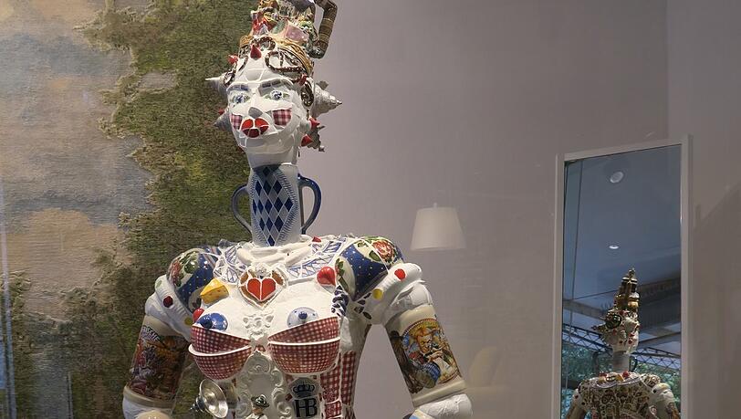 Die Wiesn kunstvoll in Szene gesetzt: Die mannshohe Oktoberfest-Figur hat nicht nur Arme und einen Hals aus Bierkrügen. Gestaltet aus Tassen und Tellern entdeckt man im Mosaik-Dirndl auch Fahrgeschäfte.