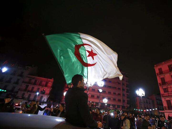 Ein Algerier schwenkt eine Nationalflagge, während Menschen feiern, nachdem Präsident Bouteflika angekündigt hat, dass er auf eine weitere Kandidatur verzichtet.