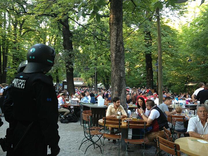 USK-Beamte (in dunkelblauen Overalls) stürmen in den Biergarten, um die Raufbolde zu trennen.