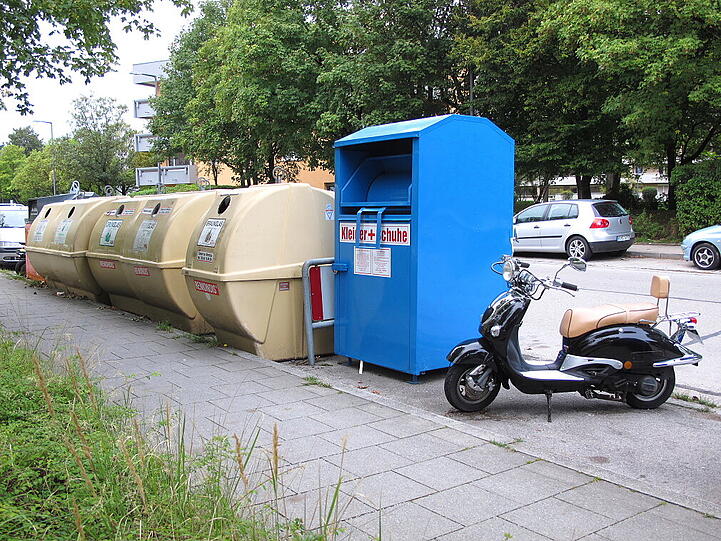 Der Roller steht neben einem Kleidercontainer.