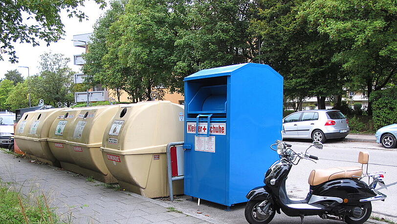 Der Roller steht neben einem Kleidercontainer. Der Roller steht neben einem Kleidercontainer.