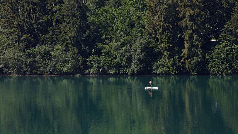 Eine Frau paddelt auf einem Stand-up Paddle Board über den Forggensee. Eine Frau paddelt auf einem Stand-up Paddle Board über den Forggensee.