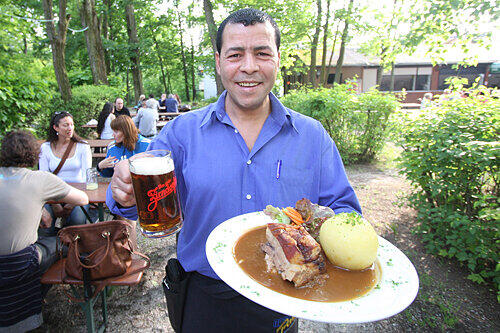 Genießen unter Bäumen: Oberkellner Kamel Msadek serviert leckeren Krustenbraten mit einem Dunklen.
