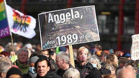 Ein Demonstrant mit Merkel-Maske trägt in Düsseldorf ein Schild mit der Aufschrift "Angela, Dein 1989 ist da!".