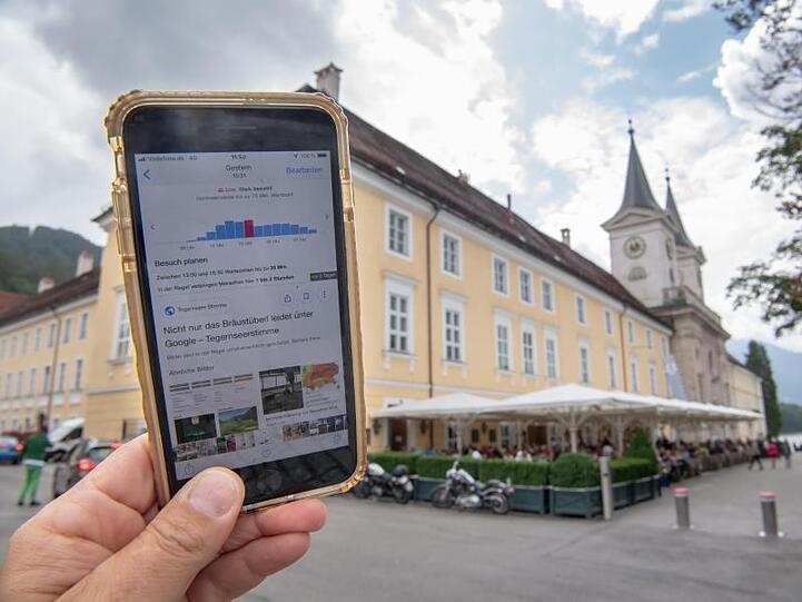 Ein Smartphone mit Angaben zu Wartezeiten wird vor dem Bräustüberl hochgehalten. Foto: Peter Kneffel/Archivbild