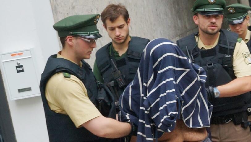 Dimosthenis C. wird abgeführt - mit einem Pullover überm Kopf. Dimosthenis C. wird abgeführt - mit einem Pullover überm Kopf.