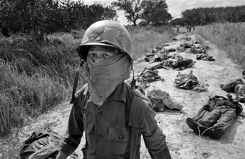 November 1965: Ein vietnamesischer Müllträger trägt eine Gesichtsmaske, um sich vor dem bestialischen Gestank zu schützen, dem er begegnet: Er passiert die leblosen Körper von US- und vietnamesischen Soldaten, die bei Kämpfen gegen den Vietcong in der Nähe der Michelin-Gummiplantage starben (rund 45 Meilen nordöstlich von Saigon).