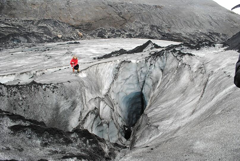 Eine Touristin kniet an einer aschebedeckten Gletscherspalte am Solheimajökull