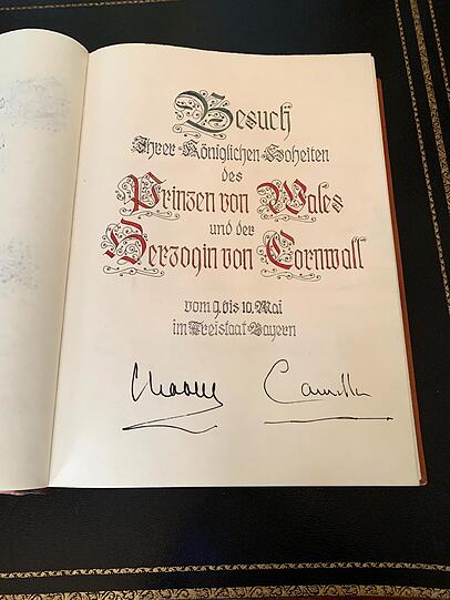 Charles und Camilla tragen sich ins Goldene Buch der Residenz ein.