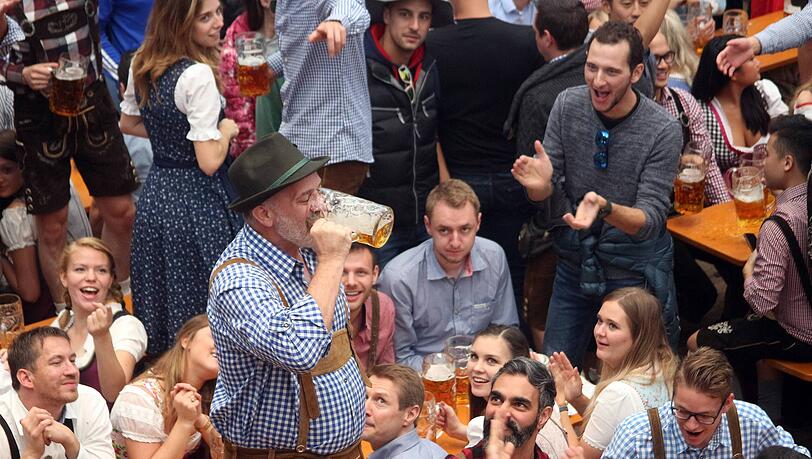 Oktoberfest München: Zeltbesucher steht auf der Sitzbank und leert seinen Maßkrug Bier in einem Zug unter dem Jubel der anderen Gäste – das sorgt normalerweise für den sicheren Rausschmiss, außer bei diesem Wiesngast.