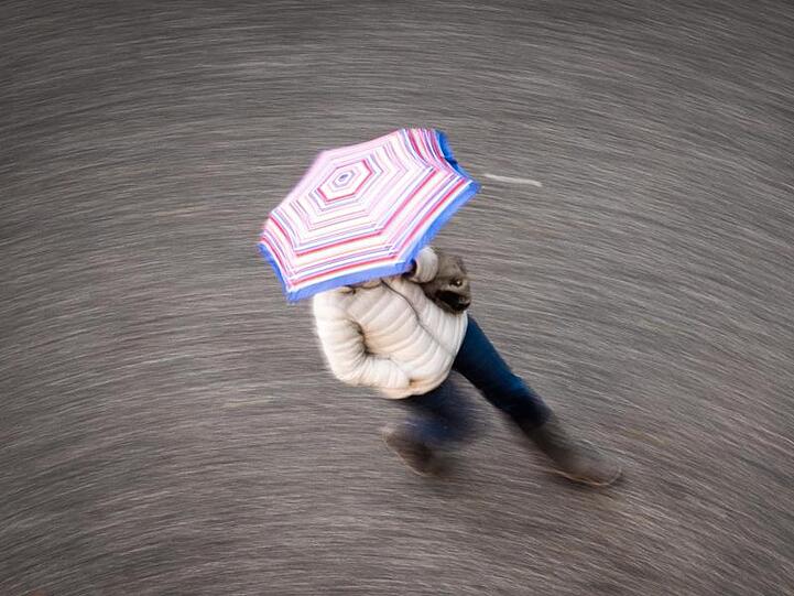 Eine Frau geht bei regnerischem Wetter über eine Straße. Foto: Frank Rumpenhorst/dpa/Symbolbild