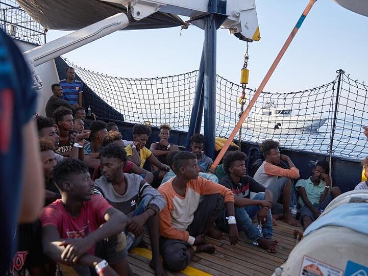 Wohin? Flüchtlinge an Bord des Seenotrettungsschiffs "Alan Kurdi", während ein Boot der italienischen Guardia di Finanza vorbei fährt.