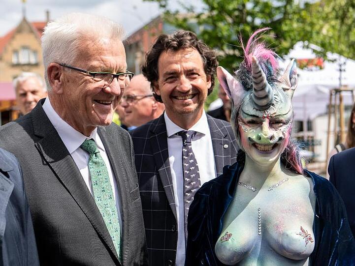 Winfried Kretschmann, Ministerpräsident von Baden-Württemberg, steht neben der als Einhorn maskierten Cynthia Schneider (Die Linke).