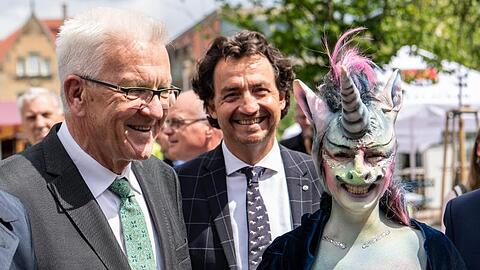 Winfried Kretschmann, Ministerpräsident von Baden-Württemberg, steht neben der als Einhorn maskierten Cynthia Schneider (Die Linke).