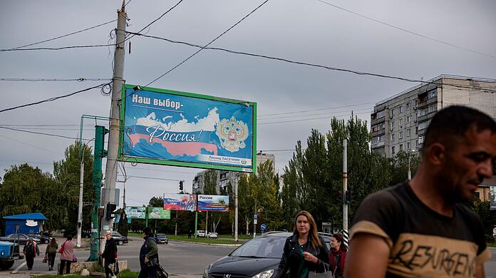 Menschen gehen in der von Russland unterstützten und von Separatisten kontrollierten Volksrepublik Luhansk in der Ostukraine an einem Plakat mit der Aufschrift "Unsere Wahl - Russland" vorbei.